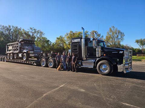 Part of the T. Disney team standing with a lowboy trailer loaded with a dump truck