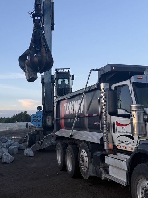 A grapple loader filling a T. Disney Trucking dump truck with large rock