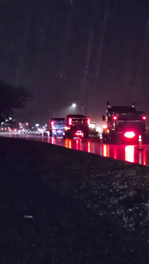 Dump trucks working a wet road at night, tail lights reflecting off the standing water