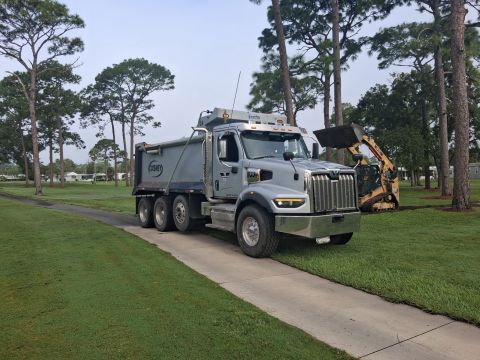A dump truck parked on dry ground beside an excavator among pine trees